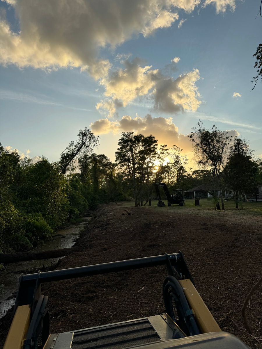 Sunset over a dirt trail with trees and a tractor bucket in the foreground