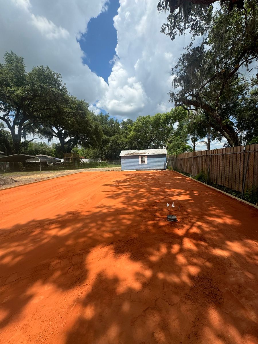 Orange dirt field with trees, a small white shed, and a bright cloudy sky.
