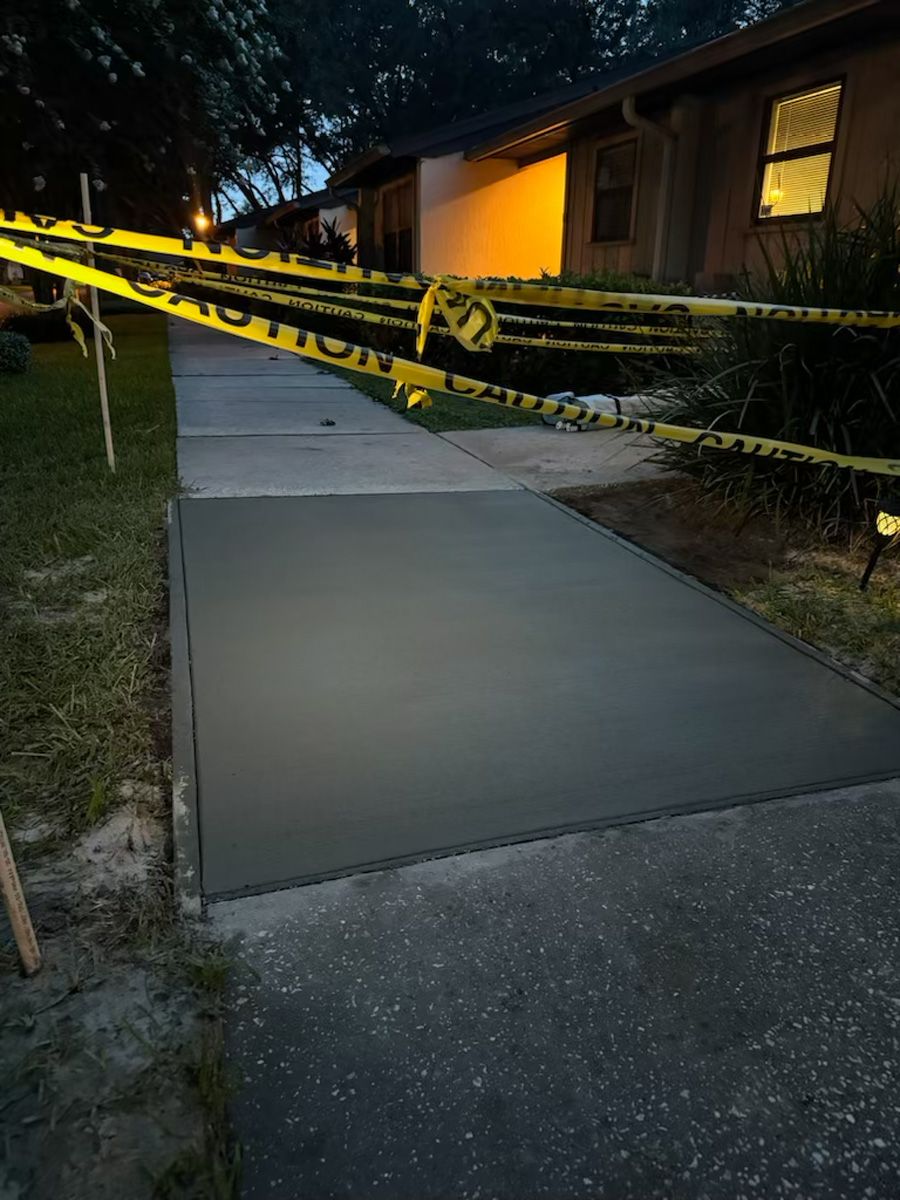 Concrete walkway behind yellow caution tape beside a house at dusk