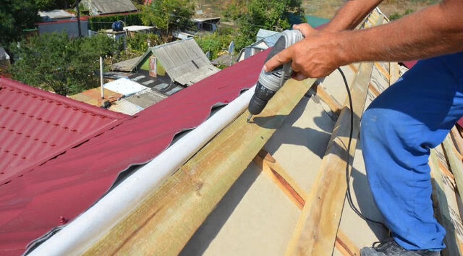 Worker sealing a rooftop seam beside a red metal roof with a caulking gun