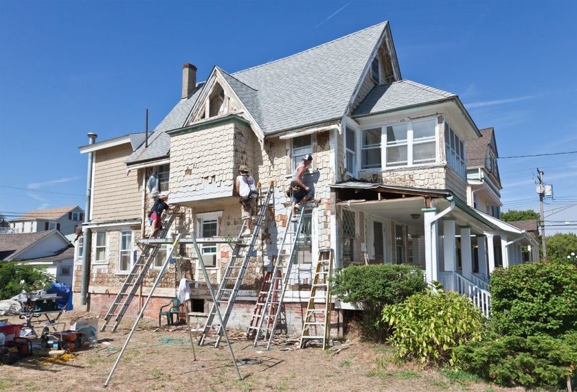 House under renovation with workers on ladders and scaffolding in front of a stone home