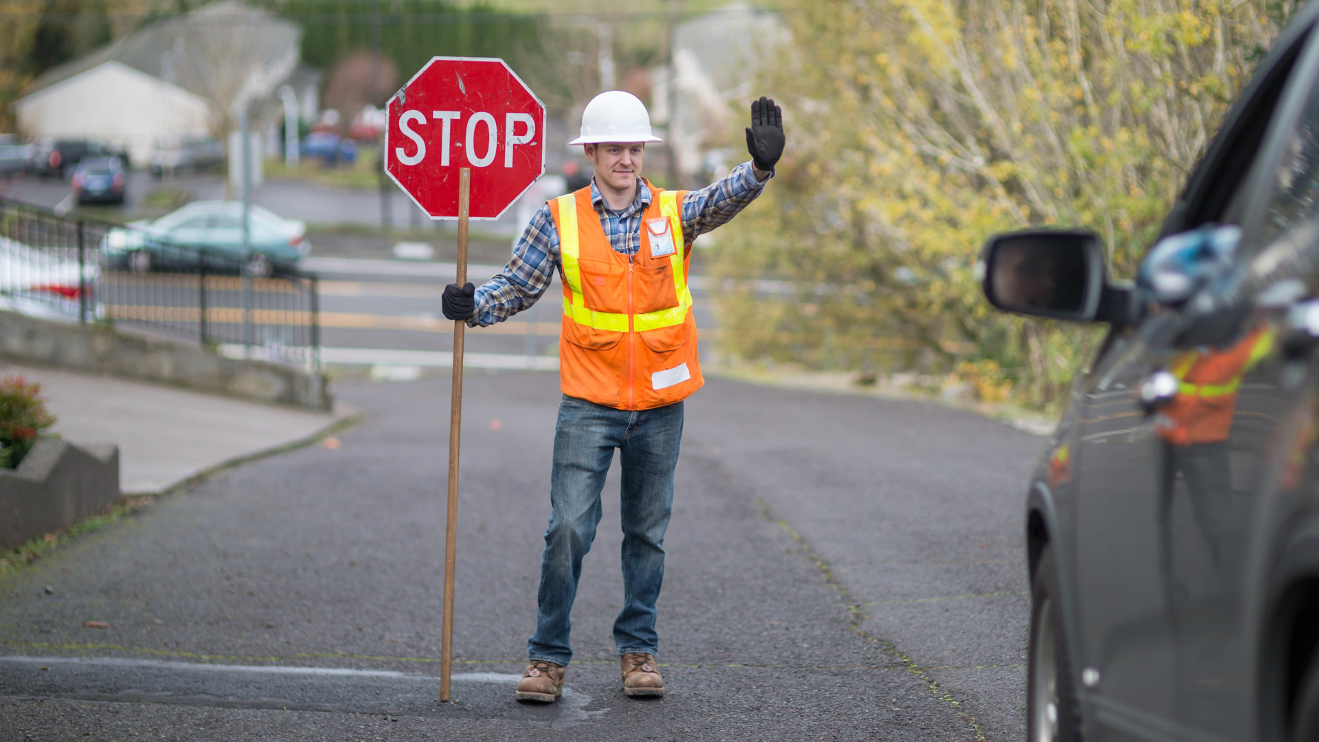 Road worker holding a stop sign, signaling a car to halt on a city street.