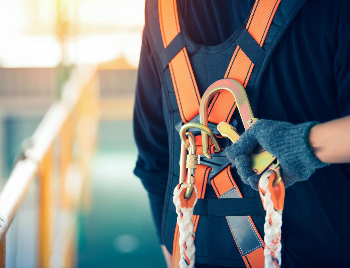 Person wearing a safety harness with orange straps, attaching a carabiner.
