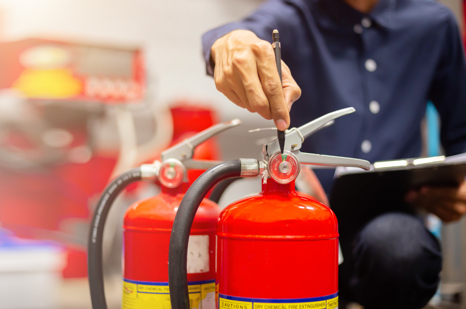 Person inspecting fire extinguishers, indoors, with clipboard and pen.