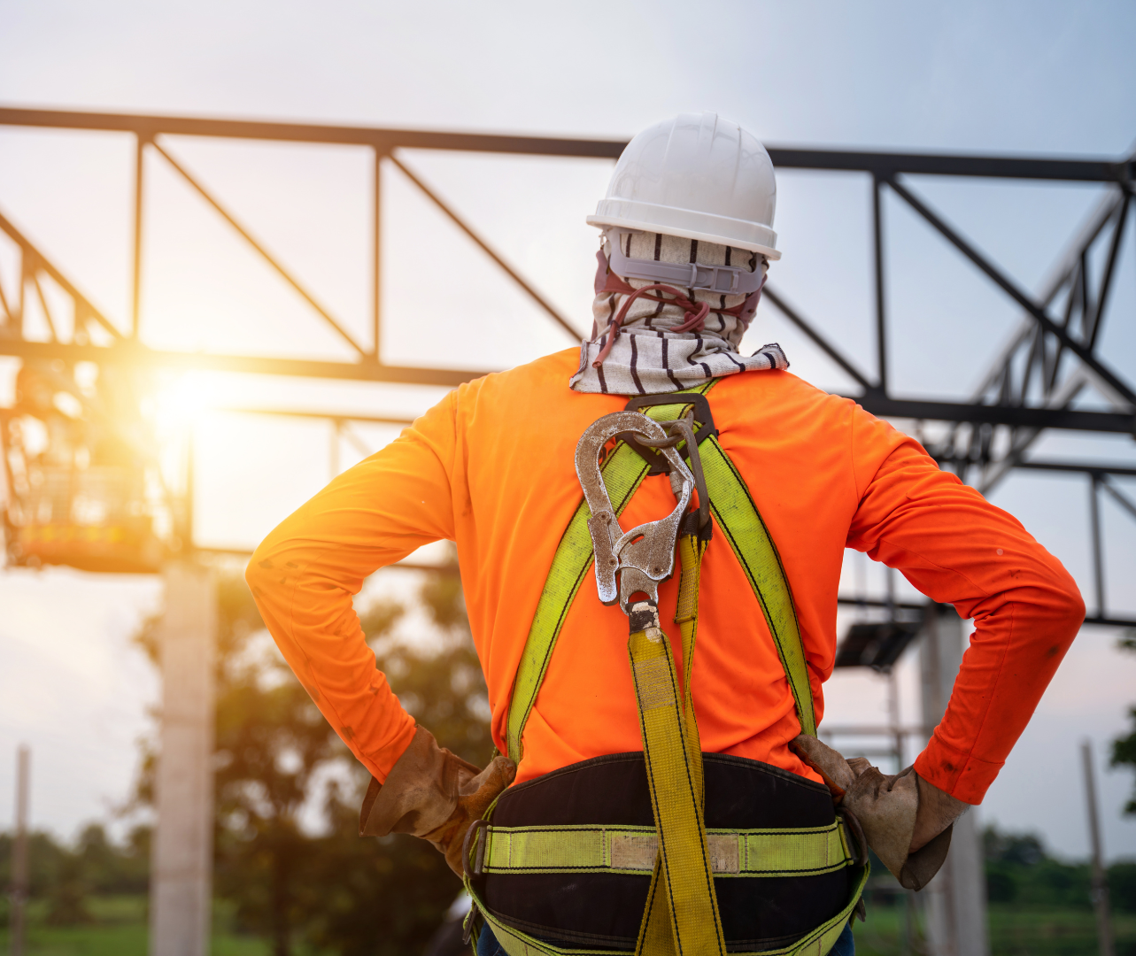 Construction worker wearing safety gear stands with hands on hips at a construction site.