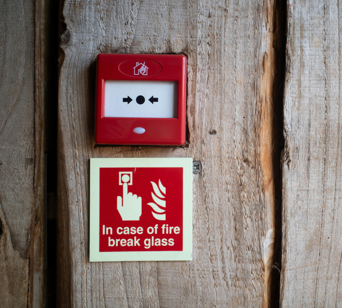Red fire alarm box and break-glass sign on a wooden wall.