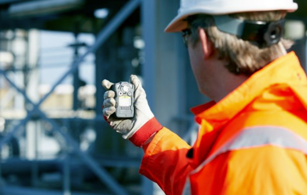 A technician in red and yellow overalls checks a boiler system, using a tablet.