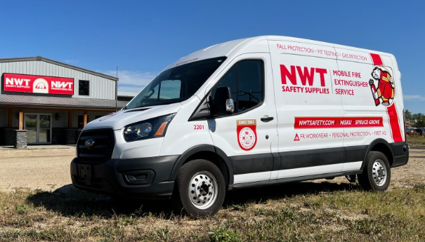 White NWT service van parked outside a red and white building under a blue sky.