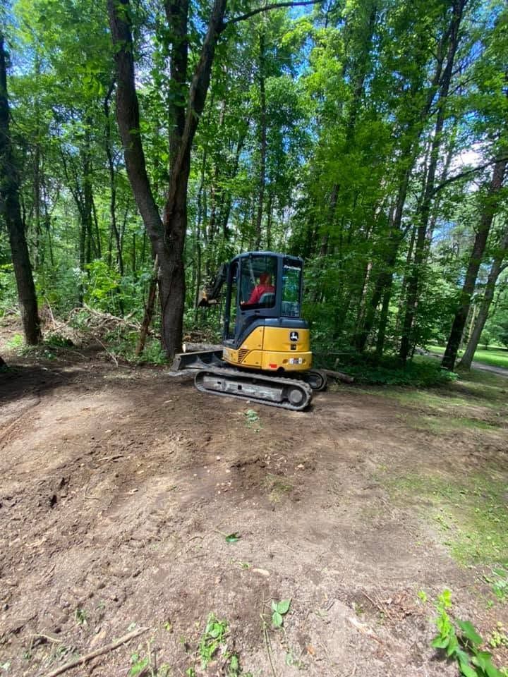 Yellow mini excavator clearing dirt in a wooded area