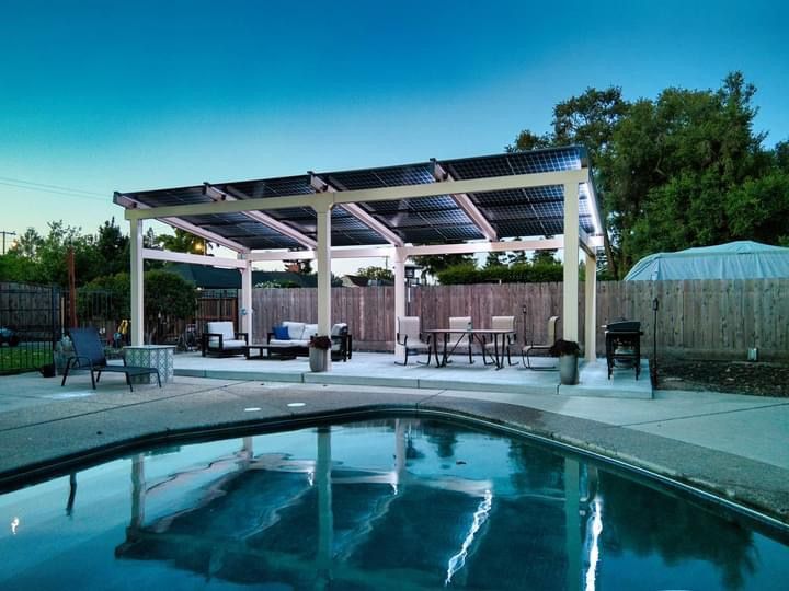 Poolside pergola with seating and dining areas; pool in foreground under a twilight sky.