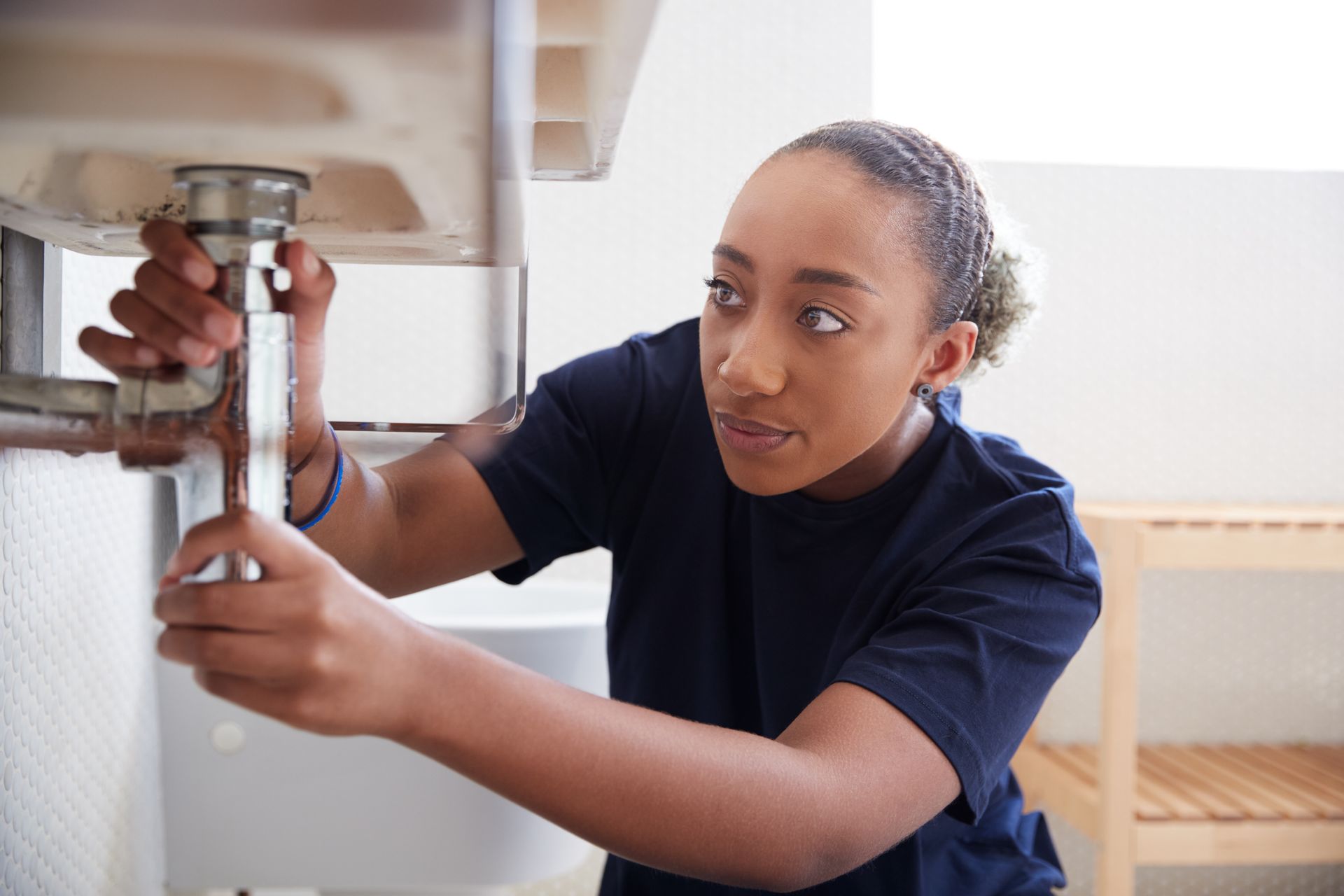 Female plumber working to fix leaking sink in home bathroom.