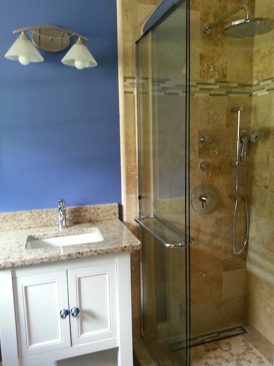 Bathroom vanity with white sink, blue wall, and glass shower with gold trim