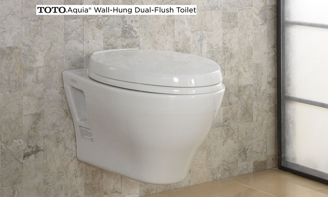 Wall-mounted white toilet in a modern bathroom with tiled walls and a window nearby