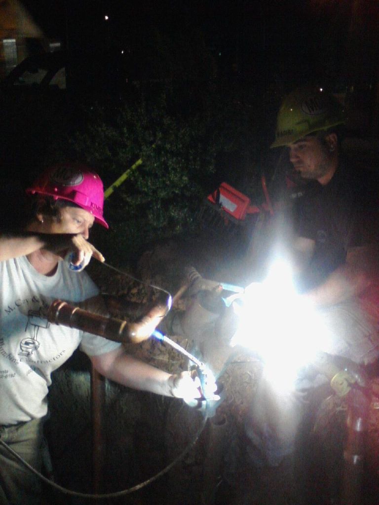 Two people in hard hats working outdoors at night with a bright flashlight or torch.