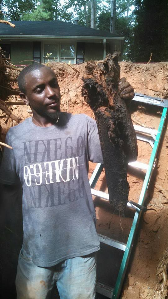 Man standing beside a ladder and a large dirt excavation site outdoors near a house
