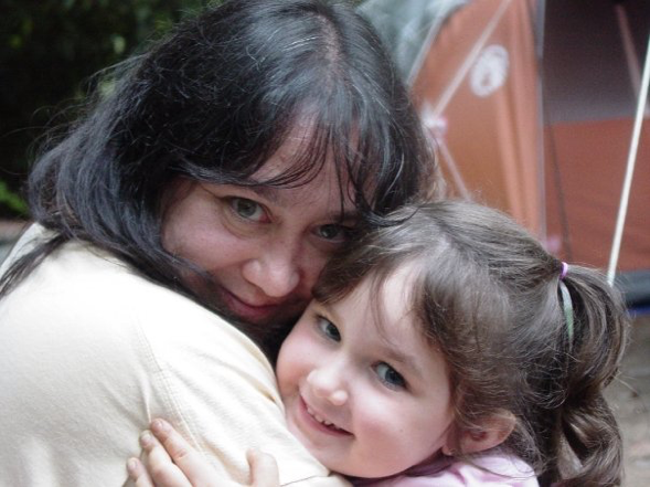 Woman hugging a smiling child indoors, both facing the camera