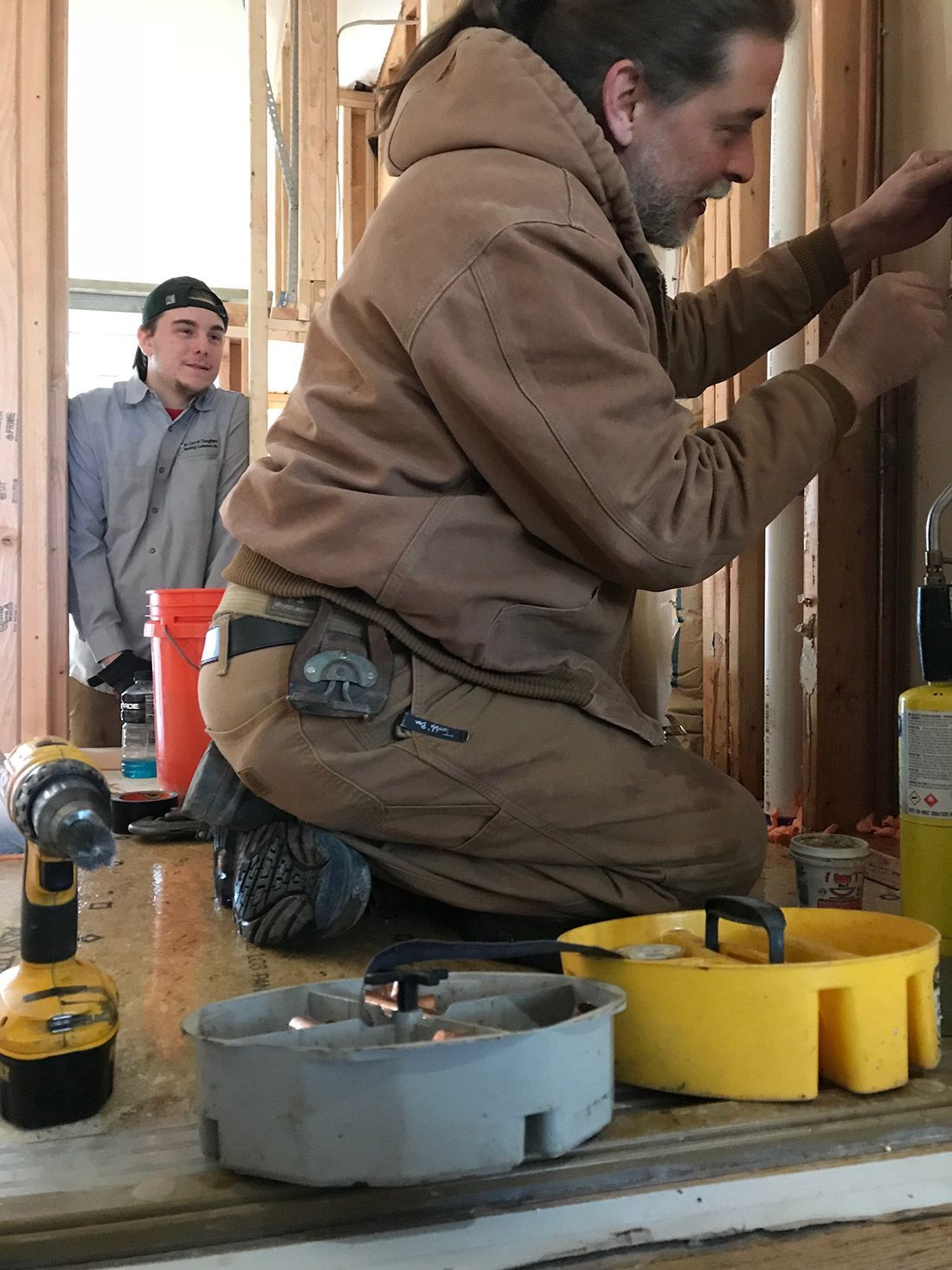 Two workers kneel at a doorway, using tools to install trim or framing at a construction site.