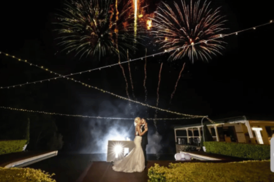 A bride and groom are kissing in front of fireworks