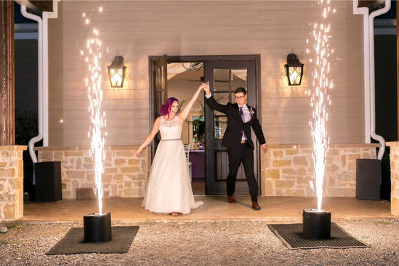 A bride and groom are standing in front of a building with fireworks.