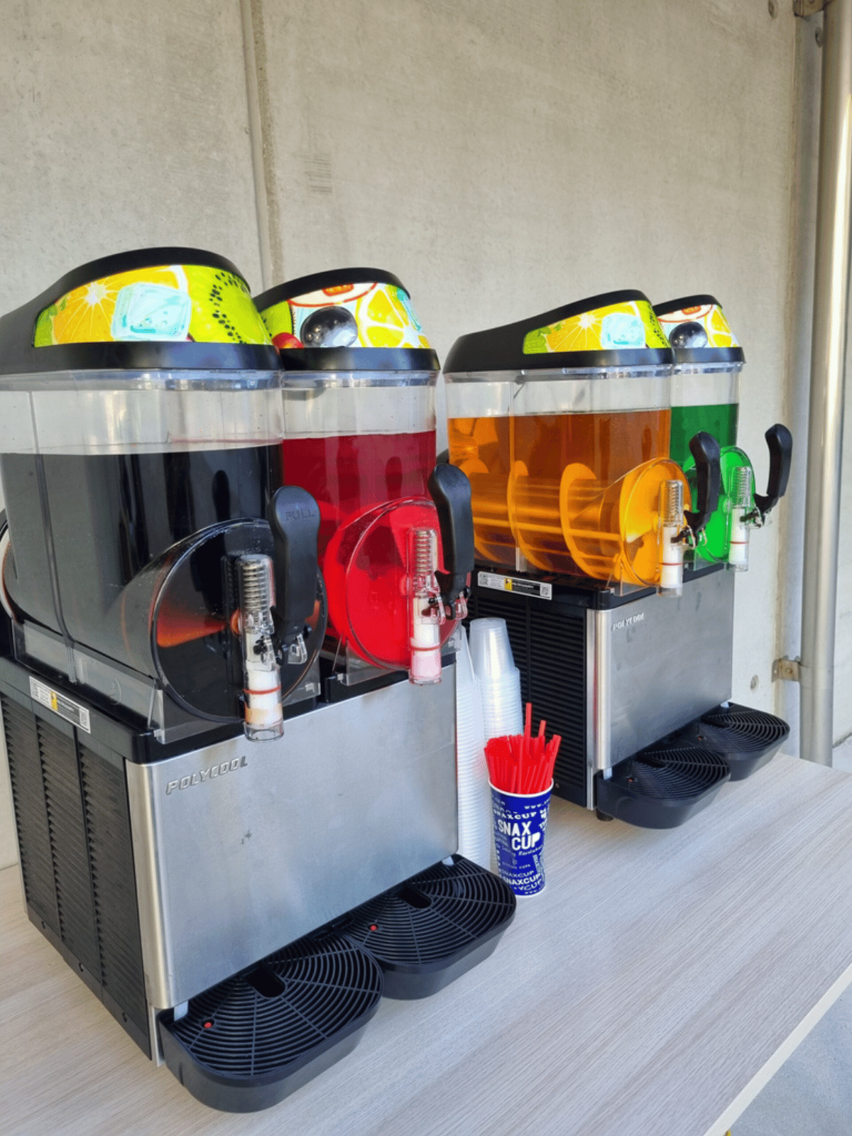 Three slushie drink dispensers are lined up on a wooden table.
