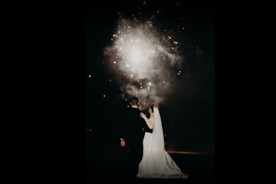 A bride and groom are kissing in front of a fireworks display.