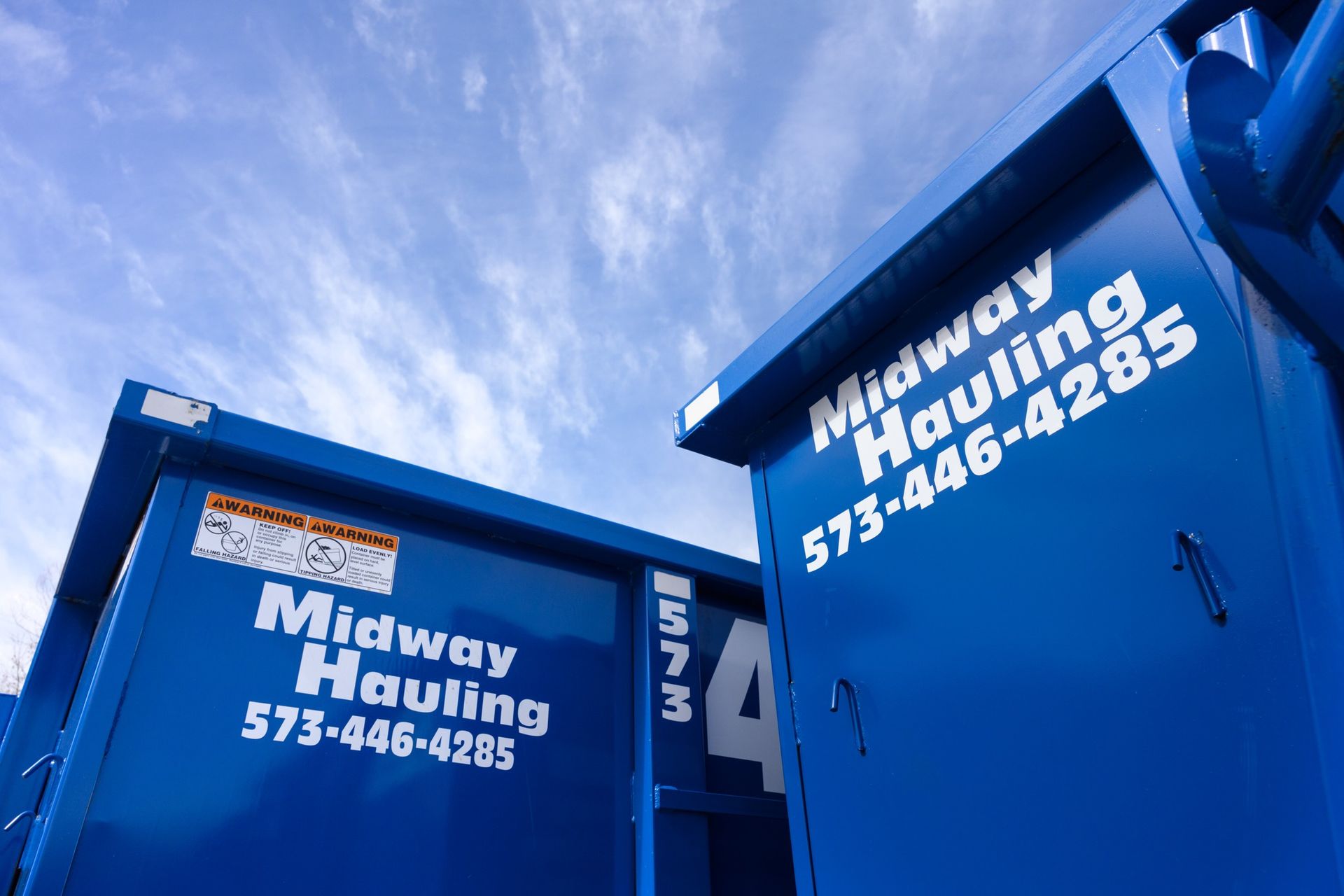 Two blue Midway Hauling dumpsters against a partly cloudy sky; phone number visible.