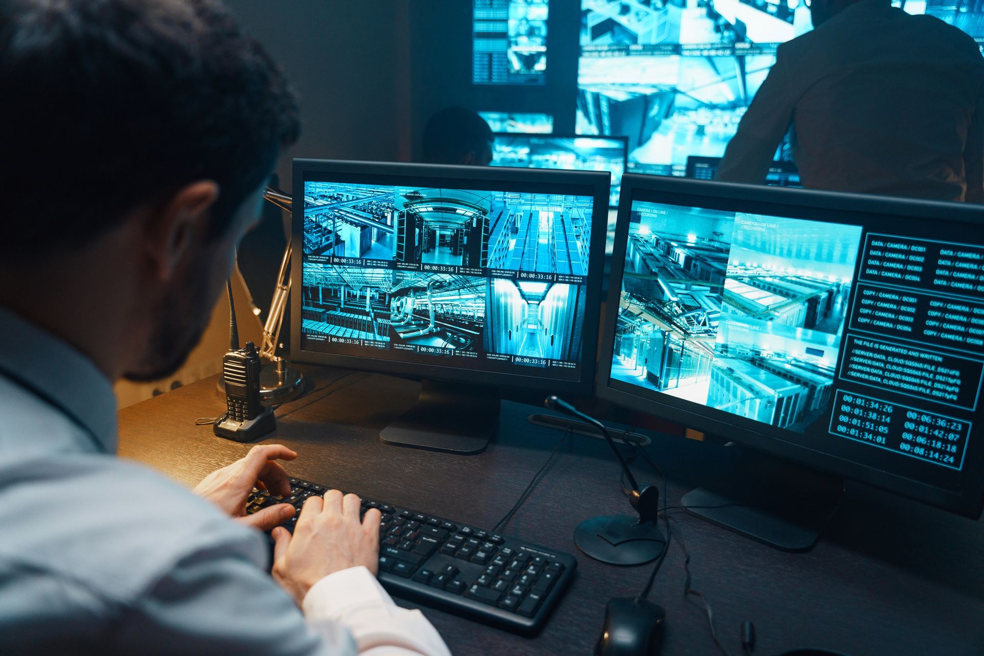 A man is typing on a keyboard in front of three computer monitors.