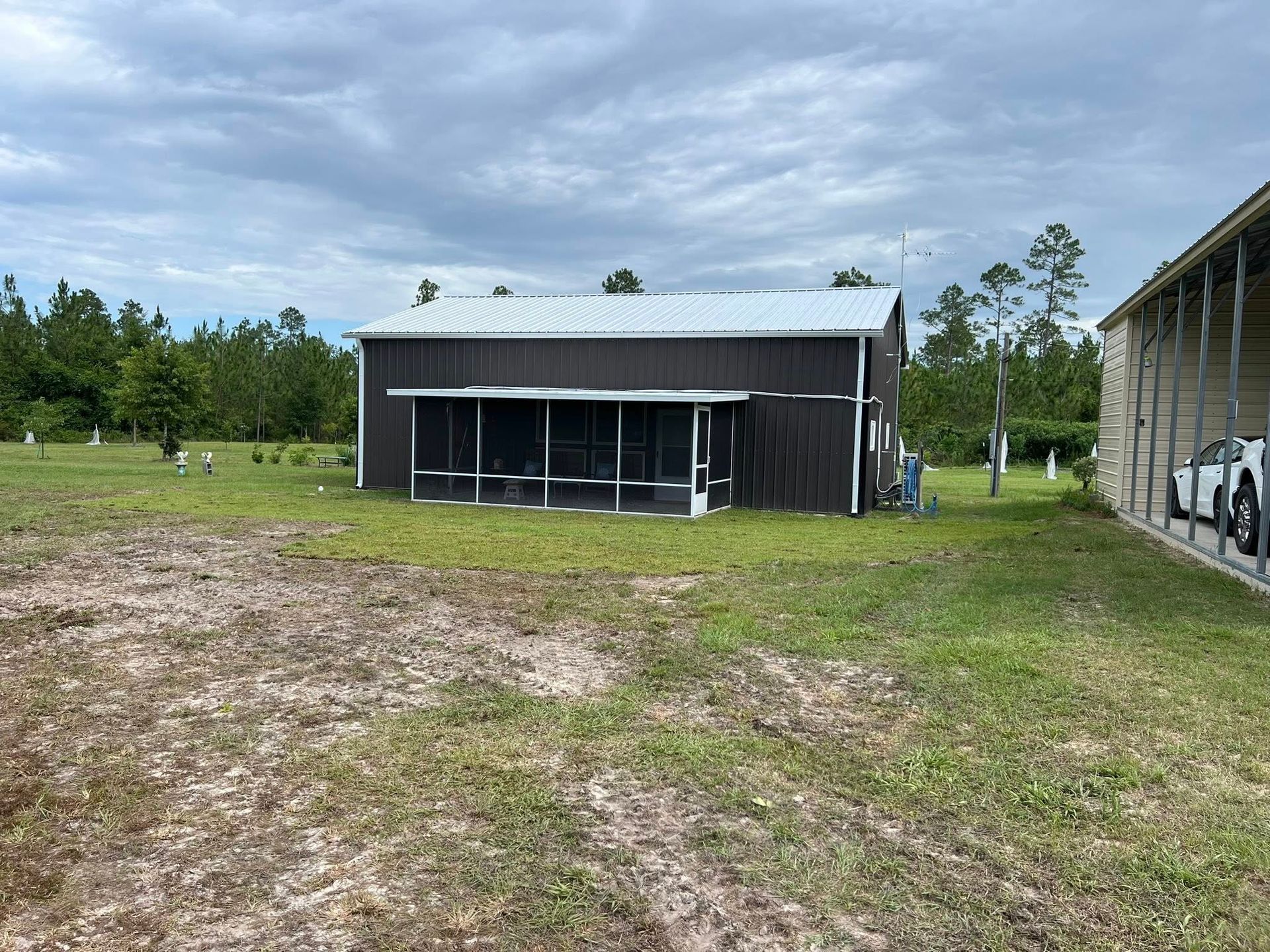 A brown metal-sided building with a screened-in porch, situated on a grassy lot under a cloudy sky.
