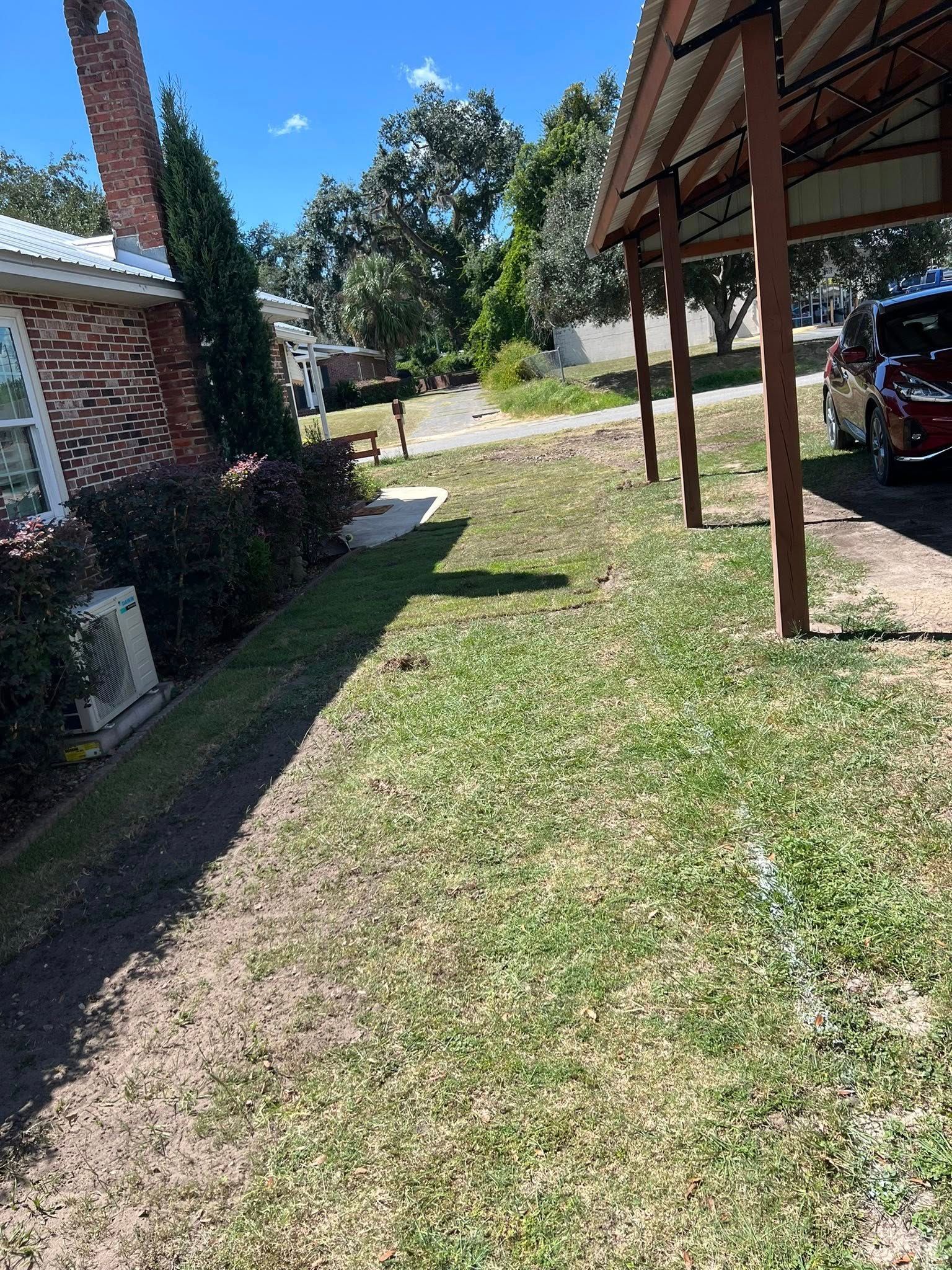 A brick house side exterior next to a grassy yard and a covered wooden carport with a parked vehicle.