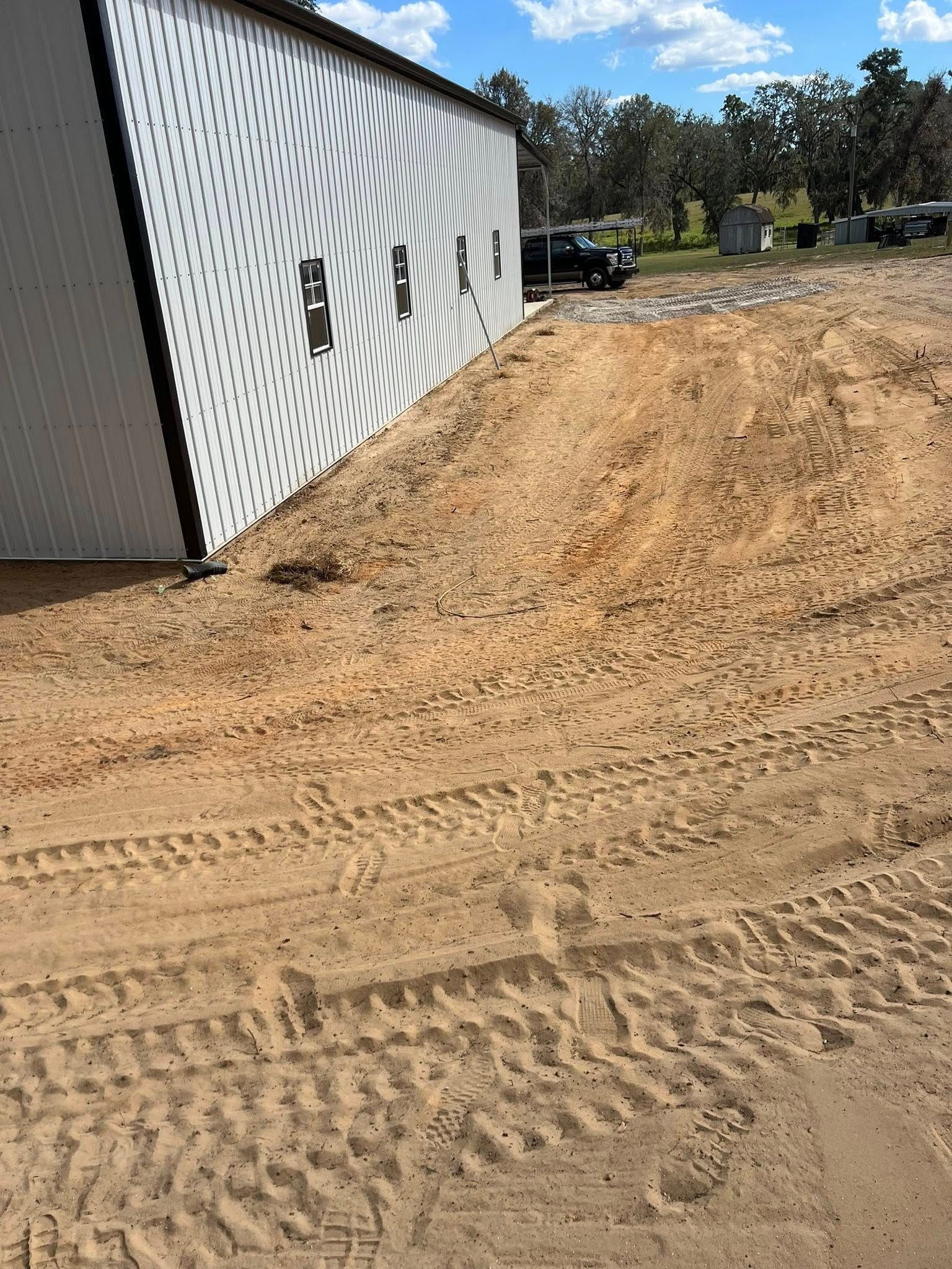 A white metal building with a repeating wave pattern on the side stands next to an area of cleared, sandy construction dirt.