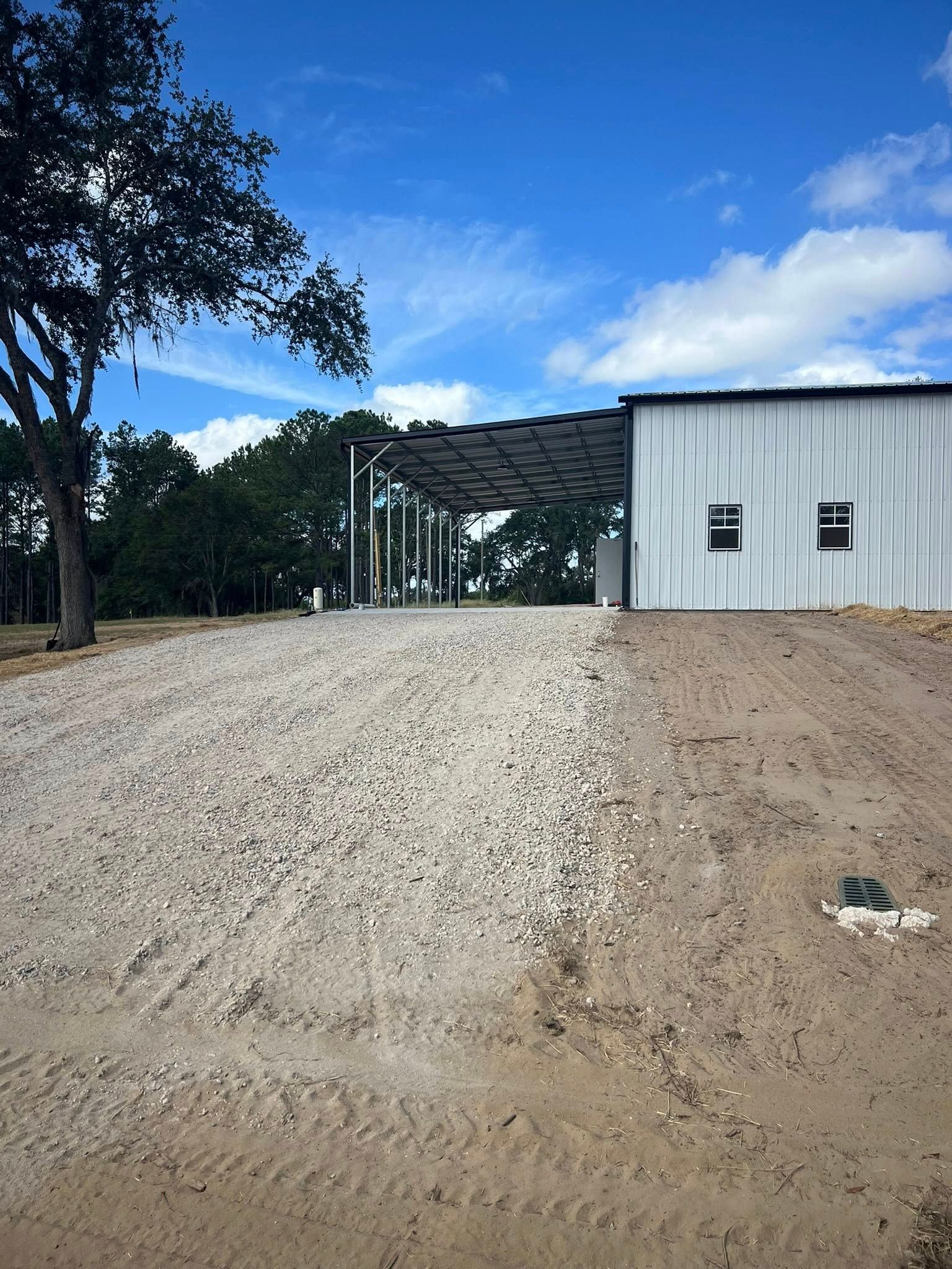 A white metal building with an attached carport sits next to a gravel driveway on a sunny day.