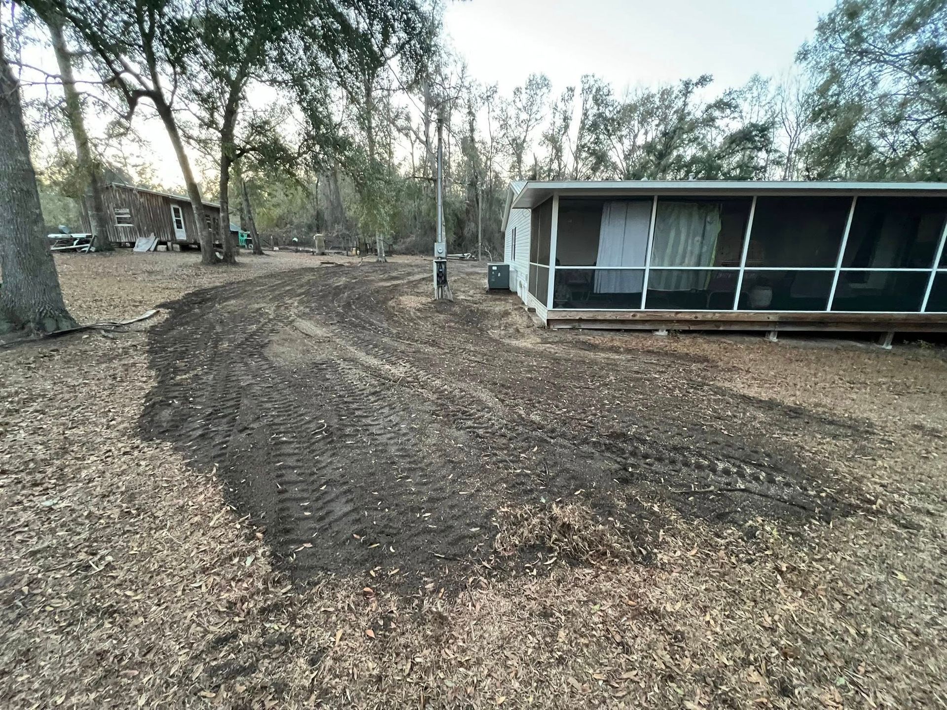 Freshly tilled dark soil in a yard next to a screened-in porch, surrounded by trees.