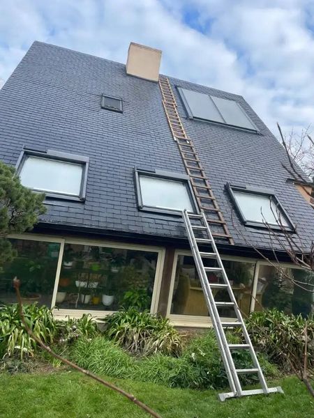 Construction workers installing gray shingles on a multi-pitched residential roof under a cloudy sky.