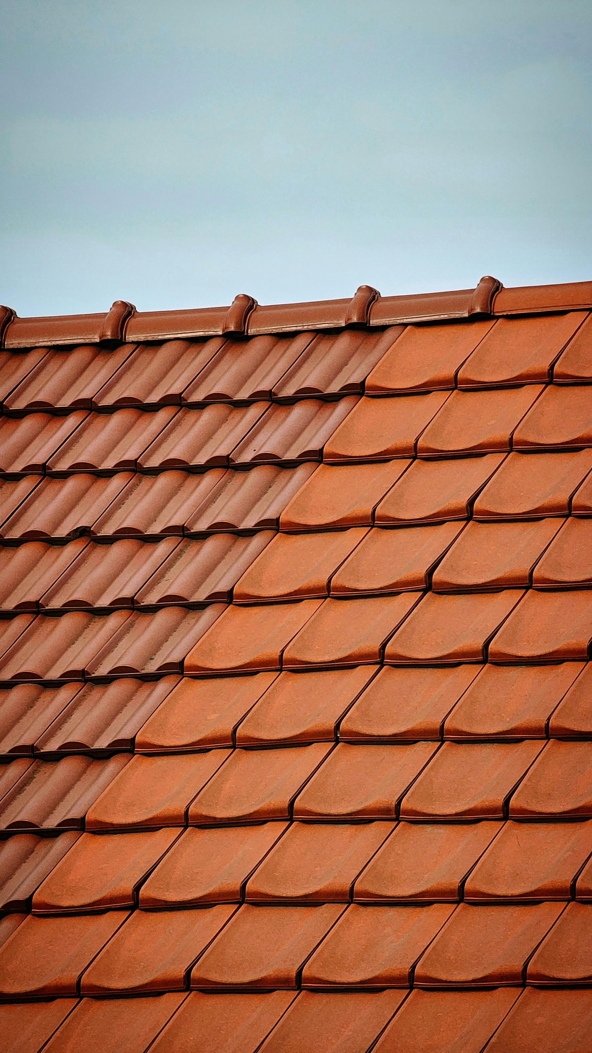 A roof covered in red clay tiles, showing a clear contrast between aged, weathered tiles and new, bright orange ones.