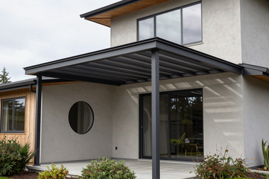 Modern house exterior with a covered patio, large glass doors, and a round window.