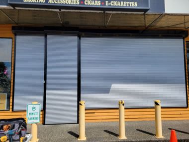 Closed storefront with gray metal shutters and yellow bollards in front