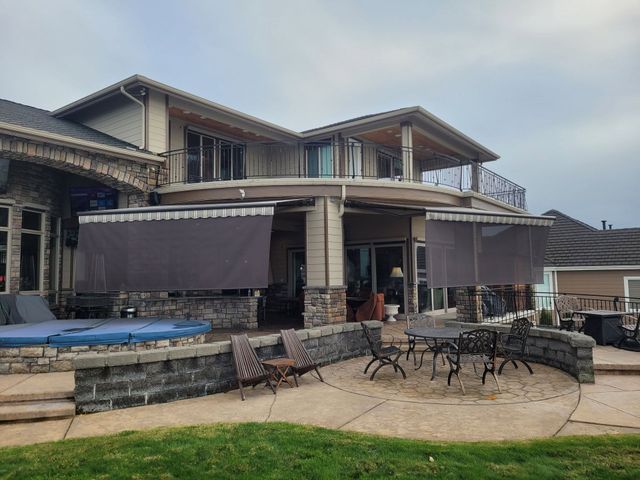 Two-story house with covered patio, hot tub, and outdoor seating on a stone terrace