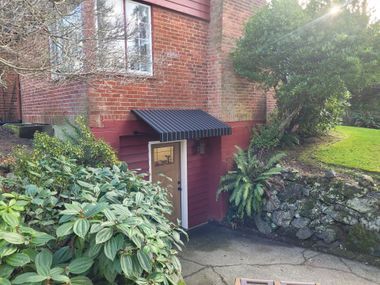 Brick house entrance with a wooden door, black awning, and stone retaining walls on both sides