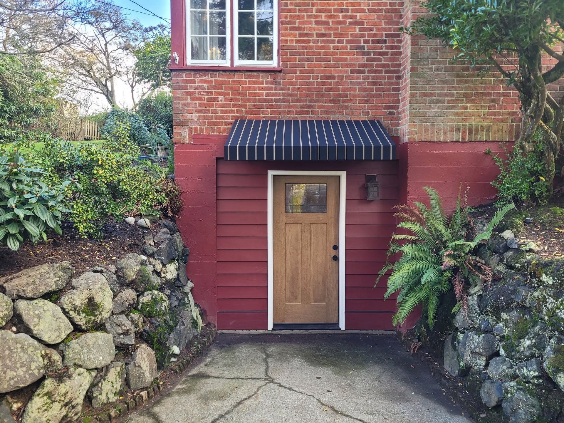 Brick house entrance with a wooden door, black awning, and stone retaining walls on both sides