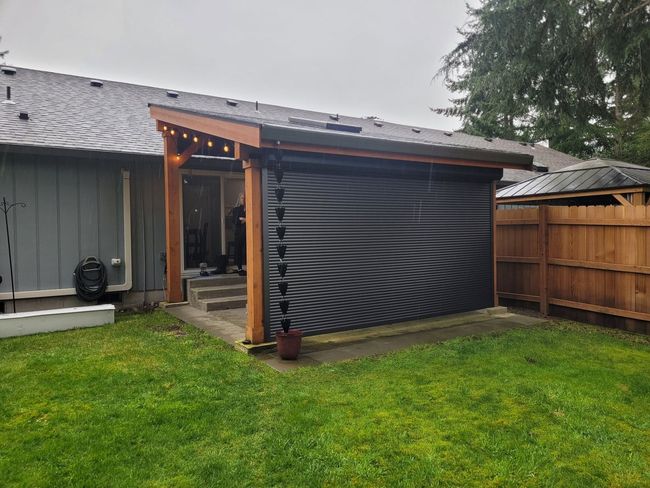 Backyard patio with a black privacy screen beside a house, surrounded by lawn and wooden fence