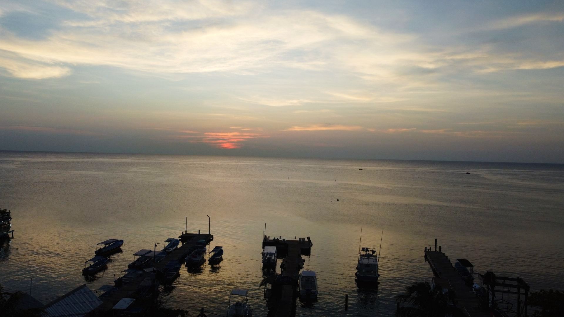 Sunset over calm water with silhouettes of docks and boats.