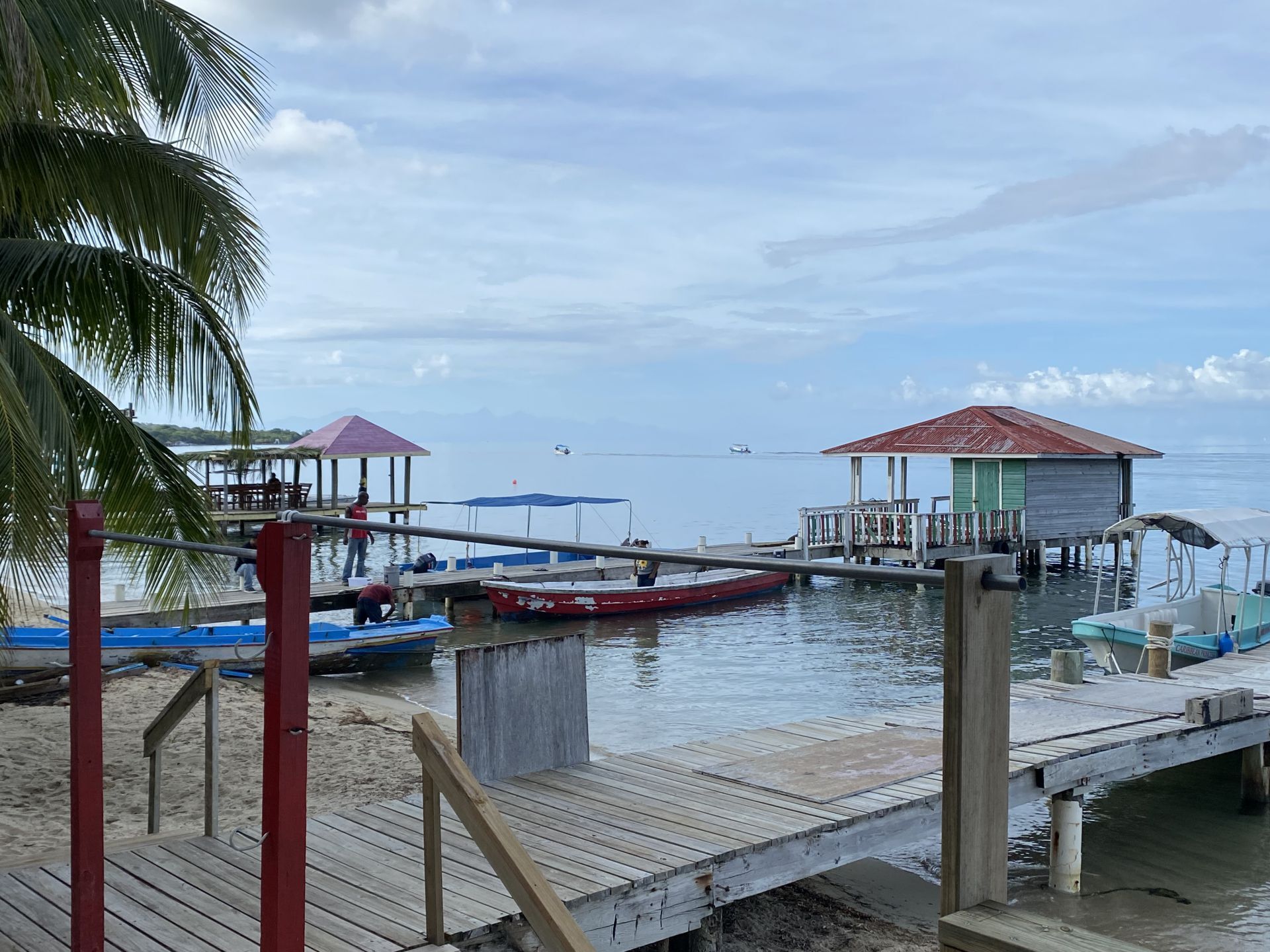 Docks and buildings on stilts over calm water; boats, beach, cloudy sky.