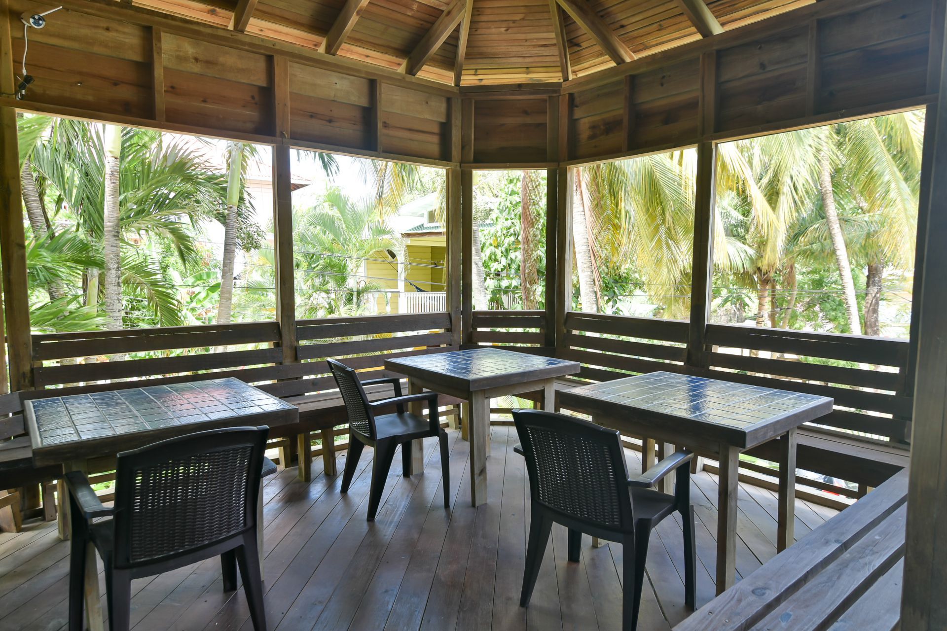 Wooden gazebo with tables and chairs, overlooking lush greenery.