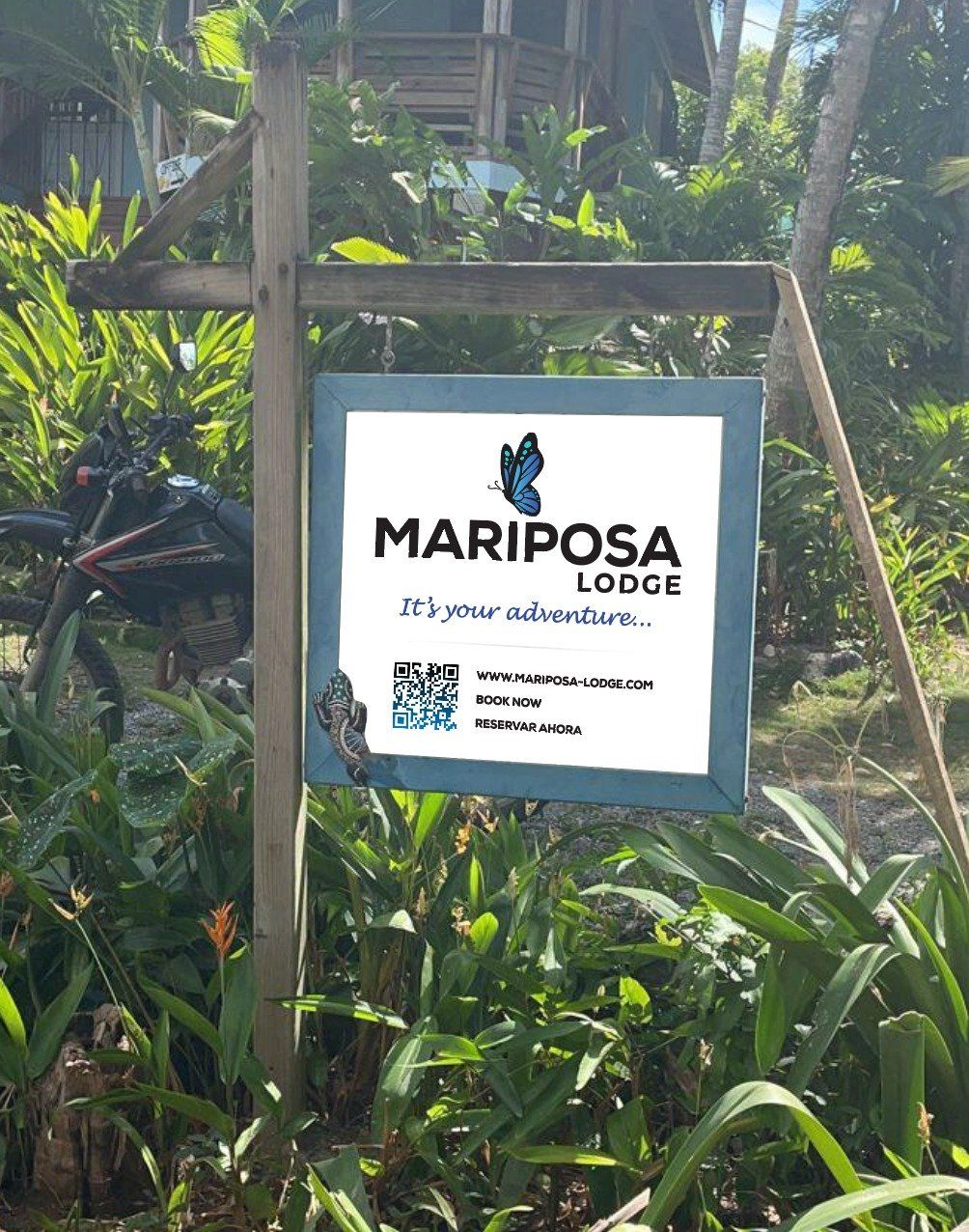 Sign for Mariposa Lodge with a butterfly logo, outdoors, surrounded by lush greenery.