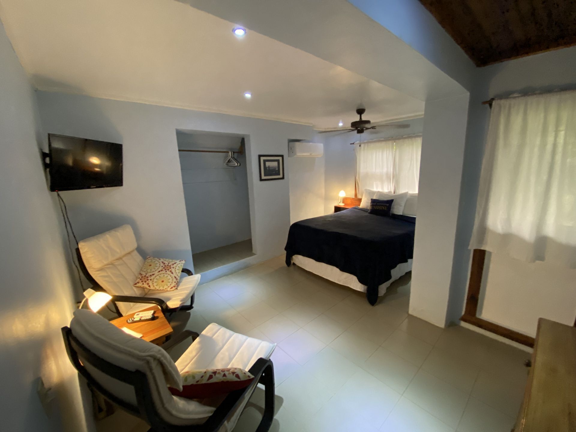Bedroom with bed, two armchairs, television, and access to a closet. Light blue walls.