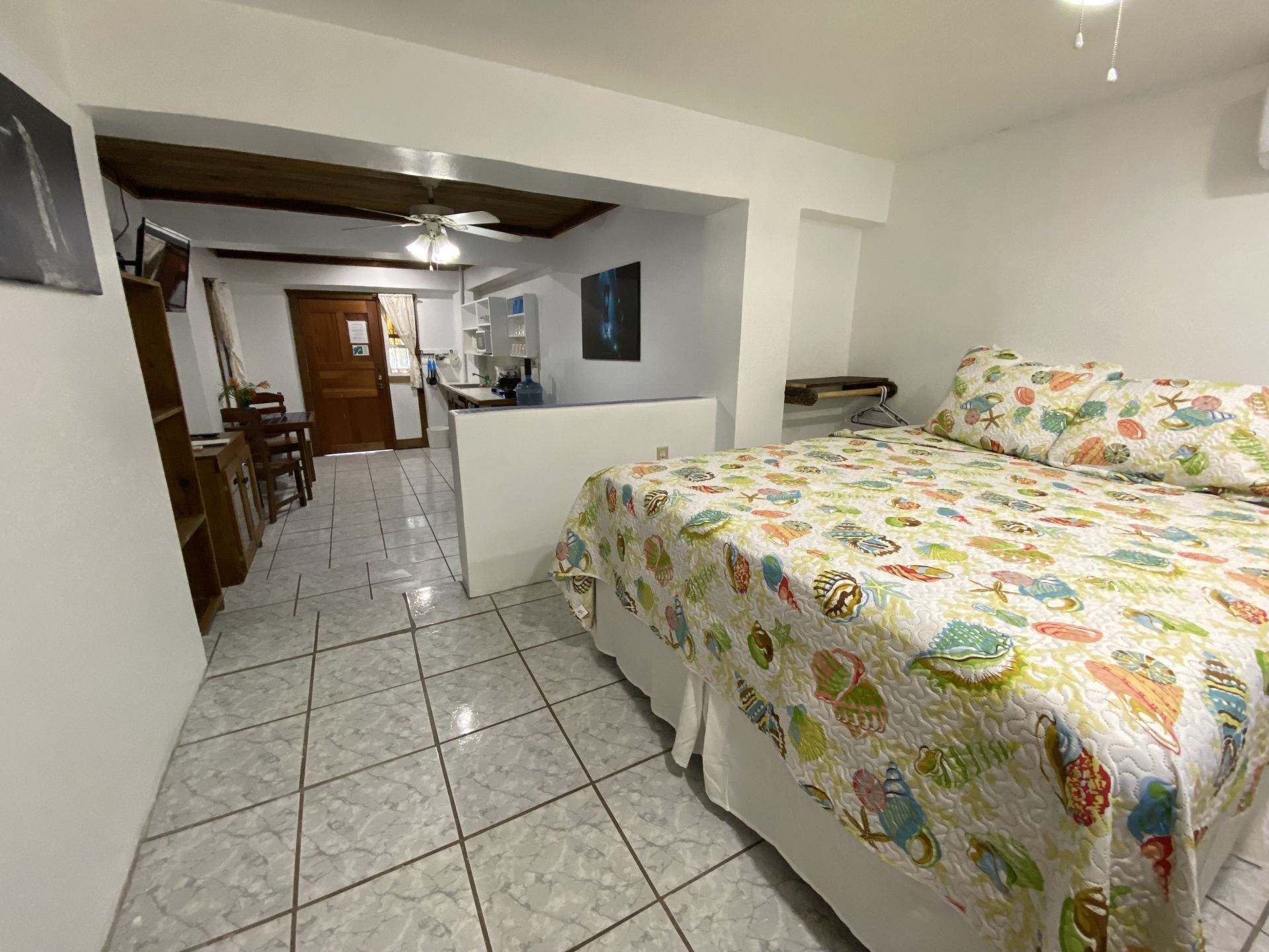 Bedroom with bed, tiled floor, opening to living space and wooden door.