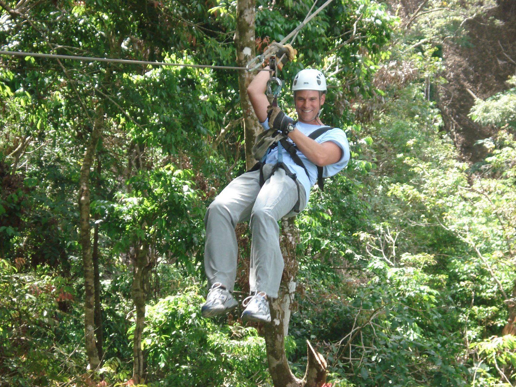 Man ziplining through a lush green forest, wearing safety gear.