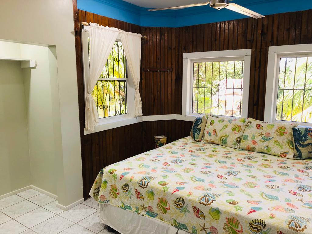 Bedroom with wood-paneled walls, bed with sea-themed bedding, windows with white frames, and a blue ceiling.