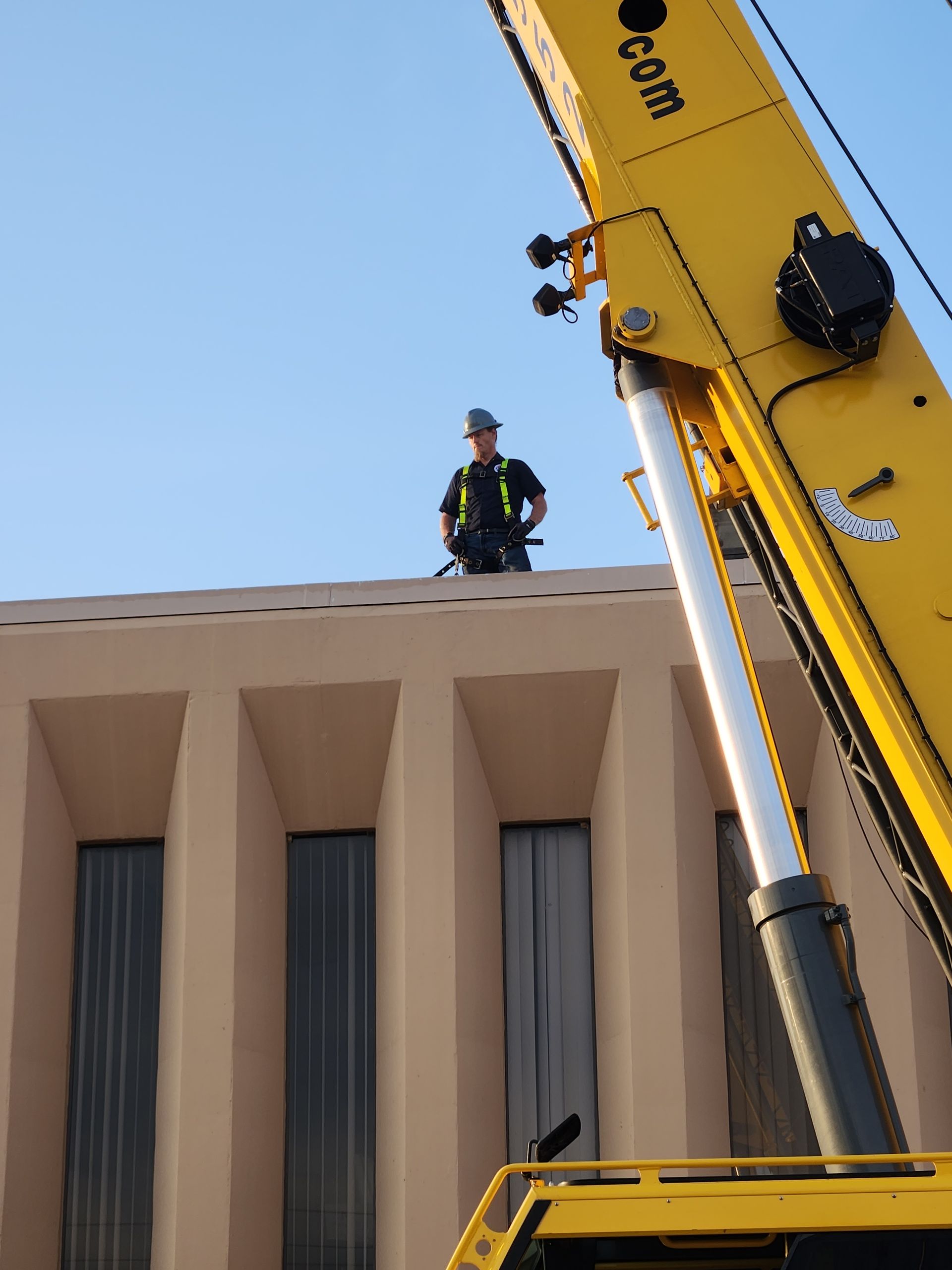 Firefighter standing on a rooftop beside a raised yellow ladder truck against a clear blue sky