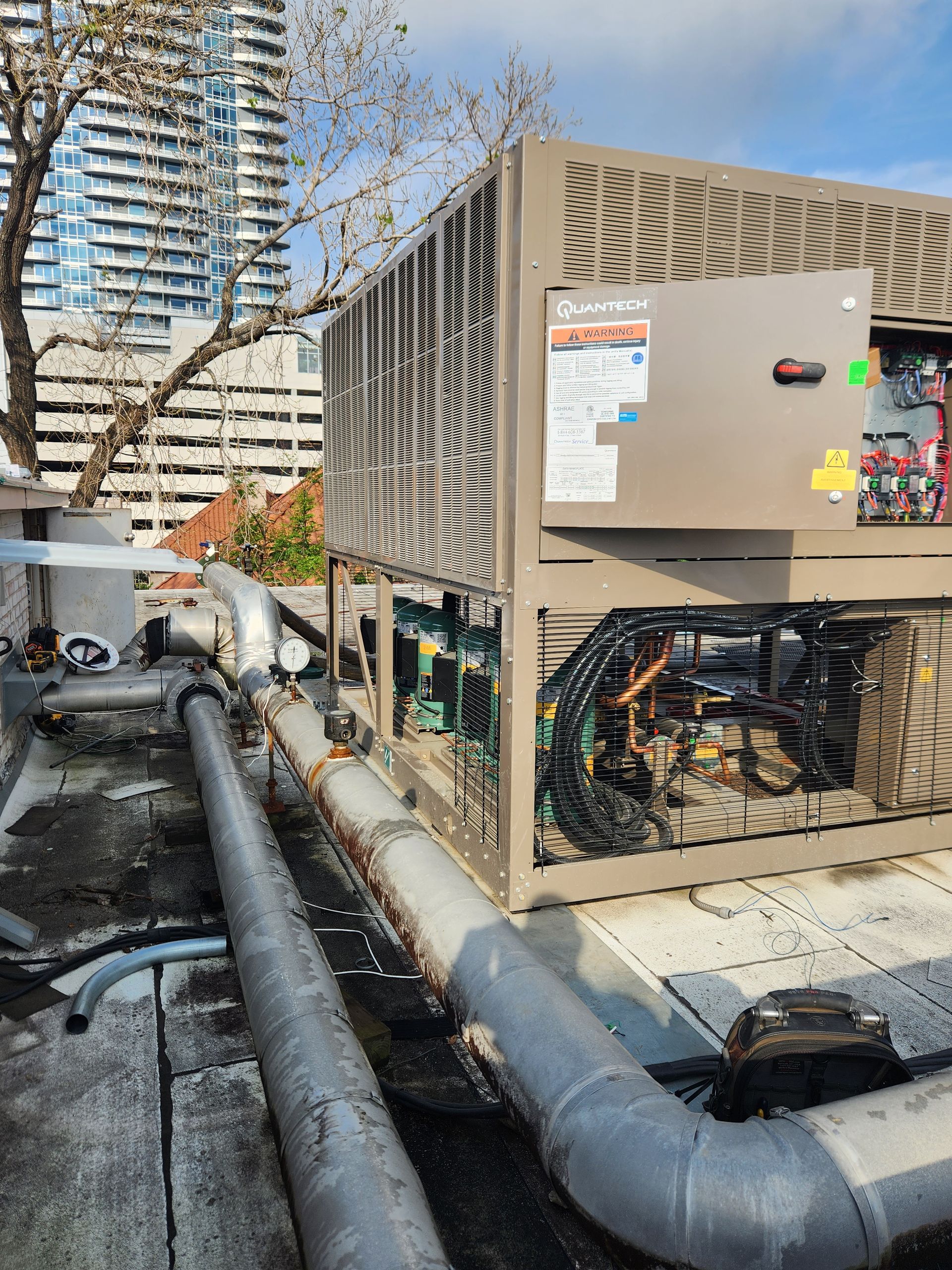 Rooftop HVAC units and large metal ductwork beside a building under a blue sky.